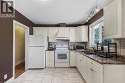 White cabinetry with integrated range hood, tile backsplash, laminate countertops, and ceramic tile flooring - 