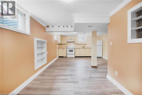 Wood-finish flooring with light-toned walls, built-in shelving, and a compact kitchen area featuring light cabinetry and white appliances - 185 Burlington Street, London, ON - Indoor Photo Showing Other Room