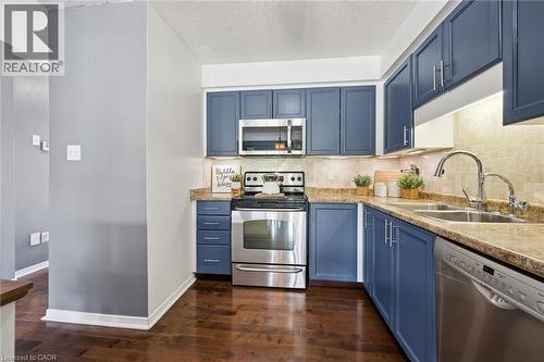 Kitchen featuring blue cabinetry, stainless steel appliances, a double basin sink, stone-finish countertops, and wood-finish flooring - 308 Parkvale Drive, Kitchener, ON - Indoor Photo Showing Kitchen With Double Sink