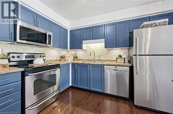 Kitchen featuring blue cabinetry, stainless steel appliances, wood-finish flooring, undermount sink, and tiled backsplash - 