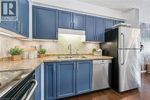 Kitchen featuring blue cabinetry, a double basin stainless steel sink, tile backsplash, stainless steel appliances, and wood-finish flooring - 308 Parkvale Drive, Kitchener, ON - Indoor Photo Showing Kitchen With Double Sink With Upgraded Kitchen