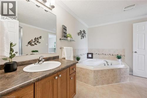 Bathroom featuring a built-in corner soaking tub with tiled surround, wood-finish vanity with an integrated sink, and an expansive mirror - 308 Parkvale Drive, Kitchener, ON - Indoor Photo Showing Bathroom