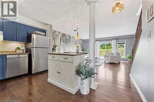 Wood-finish flooring throughout, kitchen with blue cabinetry and stainless steel appliances, white freestanding kitchen island with a wood-finish top, and a living area with sliding glass doors - 308 Parkvale Drive, Kitchener, ON - Indoor Photo Showing Kitchen