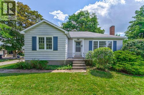 Siding exterior with blue window shutters, front entry with steps and railing, brick chimney, and mature landscaping - 321 Highland Park, Cambridge, ON 