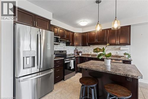 Kitchen featuring dark wood-finish cabinetry, stainless steel appliances, stone-finish countertops, and a tiled backsplash - 783 Frontenac Crescent, Woodstock, ON - Indoor Photo Showing Kitchen With Upgraded Kitchen
