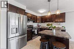 Kitchen featuring dark wood-finish cabinetry, stainless steel appliances, stone-finish countertops, and a tiled backsplash - 