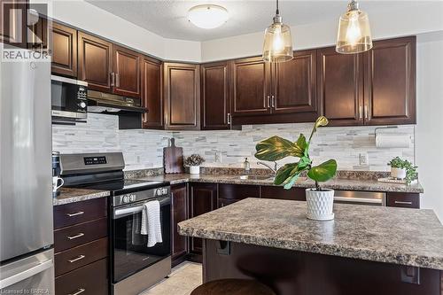 Kitchen featuring dark wood-finish cabinetry, light-toned backsplash, stainless steel appliances, and a central island with a contrasting countertop - 783 Frontenac Crescent, Woodstock, ON - Indoor Photo Showing Kitchen With Upgraded Kitchen