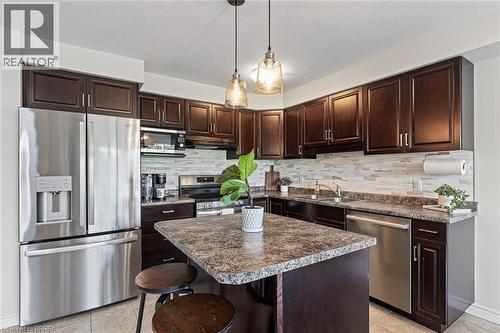 Kitchen featuring dark wood-finish cabinetry, stainless steel appliances, a center island with seating, pendant lighting, and a tile backsplash - 783 Frontenac Crescent, Woodstock, ON - Indoor Photo Showing Kitchen With Double Sink