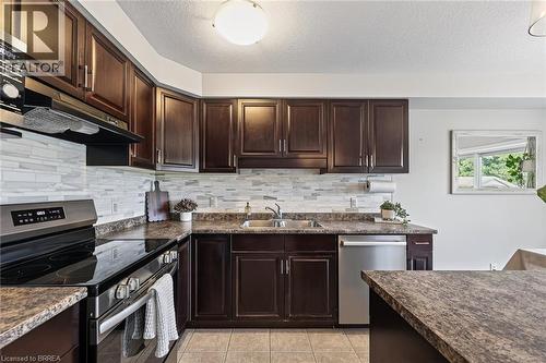 Dark wood-finish cabinetry with stainless steel hardware, mosaic tile backsplash, stainless steel appliances, and a double basin sink - 783 Frontenac Crescent, Woodstock, ON - Indoor Photo Showing Kitchen With Double Sink