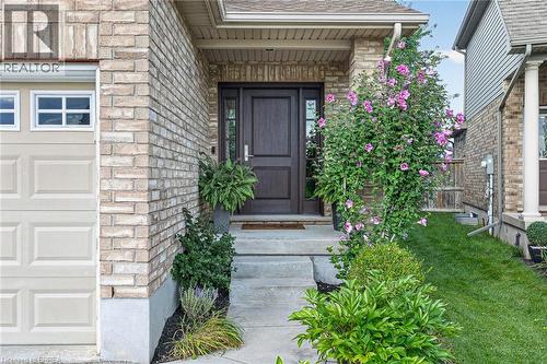 Brick exterior with a dark wood-finish entry door, garage with upper window panels, concrete steps, and lush landscaping - 783 Frontenac Crescent, Woodstock, ON - Outdoor