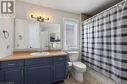 Vanity with a built-in sink and dark blue cabinetry, bronze-finish wall-mounted light fixture, large wall mirror, toilet, and tile flooring - 