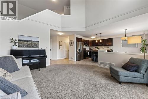 Carpeted living area with high ceilings, recessed lighting, and a partial wall separating a kitchen with dark cabinetry and stainless steel appliances - 783 Frontenac Crescent, Woodstock, ON - Indoor Photo Showing Living Room