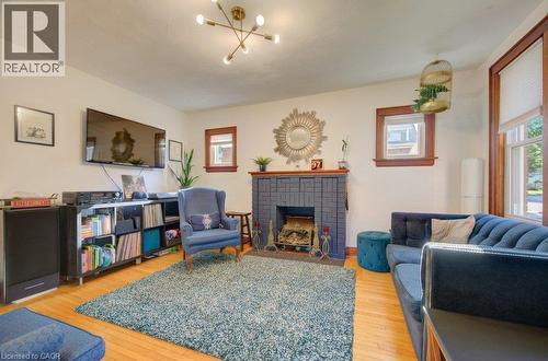 Hardwood flooring, a fireplace with a dark brick surround, warm wood trim around windows, and a modern ceiling light fixture - 97 Francis Street, Cambridge, ON - Indoor Photo Showing Living Room With Fireplace
