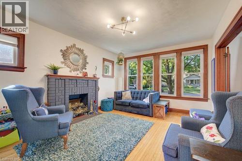 Hardwood flooring, a modern multi-bulb ceiling fixture, a substantial fireplace with a stone surround, and multiple windows with wood trim - 97 Francis Street, Cambridge, ON - Indoor Photo Showing Living Room With Fireplace