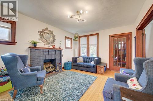 Hardwood flooring throughout, a fireplace with a stone surround, wood-trimmed windows, a wood-framed glass-paneled door, and a multi-directional ceiling light fixture - 97 Francis Street, Cambridge, ON - Indoor Photo Showing Living Room With Fireplace