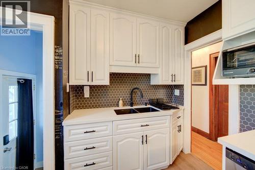 White cabinetry with matte black hardware, black hexagonal tile backsplash, white countertops, and a black double basin sink - 97 Francis Street, Cambridge, ON - Indoor Photo Showing Kitchen With Double Sink