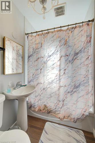 Pedestal sink with chrome faucet, shower/tub combination, wood-finish flooring, and a decorative chandelier - 97 Francis Street, Cambridge, ON - Indoor Photo Showing Bathroom
