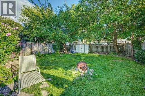 Expansive backyard featuring a green lawn, mature trees, wood fencing, a stone fire pit, and a storage shed - 97 Francis Street, Cambridge, ON - Outdoor With Backyard