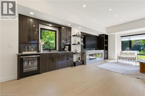 Integrated wet bar with dark wood-finish cabinetry, built-in beverage refrigerator, and sink - 282 Robina Road, Ancaster, ON - Indoor With Fireplace