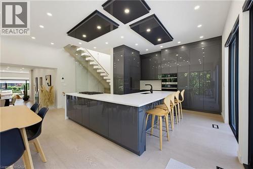 Modern kitchen featuring a large central island with a white countertop and integrated cooktop, glossy gray cabinetry, recessed lighting, and wood-finish flooring - 282 Robina Road, Ancaster, ON - Indoor