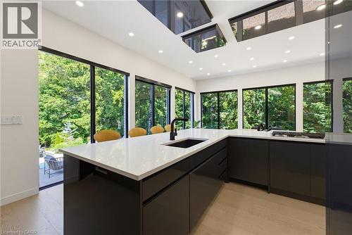 Modern kitchen featuring expansive windows, recessed lighting, sleek black cabinetry, a white countertop island with an integrated sink, and wood-finish flooring - 282 Robina Road, Ancaster, ON - Indoor Photo Showing Kitchen