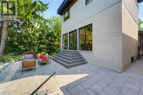 Expansive paver patio with a glass railing system, leading to a modern exterior with light brick and large black-framed windows - 282 Robina Road, Ancaster, ON - Outdoor With Exterior