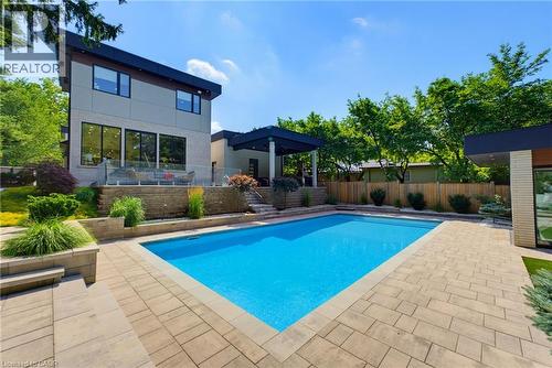 Rectangular swimming pool with surrounding paver patio and tiered landscaping - 282 Robina Road, Ancaster, ON - Outdoor With In Ground Pool With Backyard