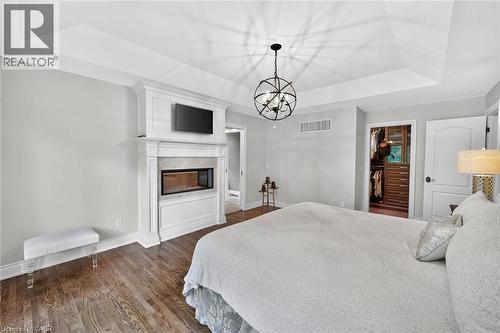 Tray ceiling with a spherical chandelier, wood-finish flooring, white mantel, built-in fireplace, and an open closet with built-in shelving - 11 Christman Court, Markham, ON - Indoor Photo Showing Bedroom