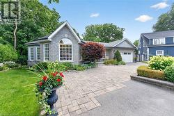 Stone facade with a prominent arched window, bay window, paver driveway, attached garage, and landscaped garden beds - 