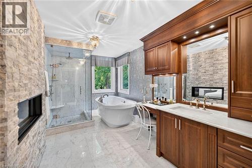 Spacious bathroom featuring a freestanding tub, glass-enclosed shower, stone accent wall with built-in fireplace, and a wood-finish vanity with countertop sink - 11 Christman Court, Markham, ON - Indoor Photo Showing Other Room