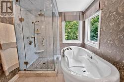 Freestanding soaking tub, walk-in shower with glass enclosure, integrated shower bench, dual windows, and ornate patterned wallpaper - 