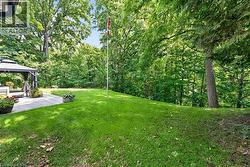 Expansive backyard featuring a manicured lawn, established trees, and a stone paver patio with a built-in gazebo - 