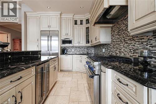 Kitchen featuring built in appliances, stone tile floors, beverage cooler, dark stone countertops, and ornamental molding - 205 Paige Place, Kitchener, ON 