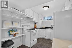 Lower-level kitchen with subway tile backsplash, white cabinetry, dark countertops, a double basin stainless steel sink, and luxury vinyl flooring - 