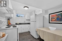 Lower-level kitchen with subway tile backsplash, white cabinetry, dark countertops, a double basin stainless steel sink, and luxury vinyl flooring - 