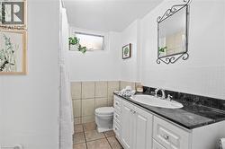 3-piece lower level bathroom featuring a white vanity with a dark countertop, ceramic tiles and a decorative wall mirror - 