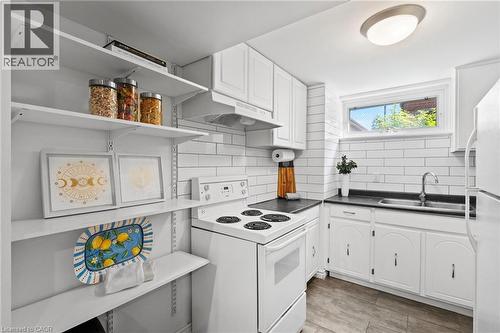 Lower-level kitchen with subway tile backsplash, white cabinetry, dark countertops, a double basin stainless steel sink, and luxury vinyl flooring - 1083 Melton Drive, Mississauga, ON 