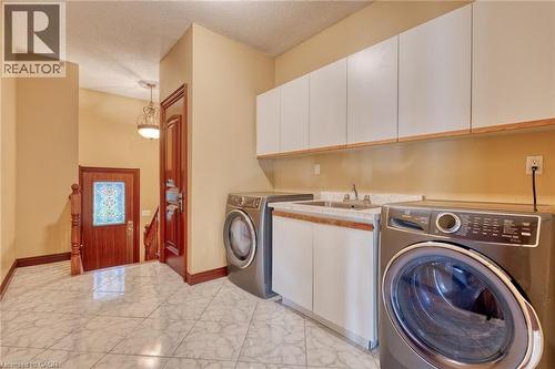 Laundry area with white cabinetry, a utility sink, and stone-look countertops, complemented by tile flooring - 23 Susan Drive, Hamilton, ON 