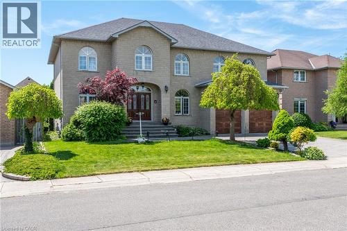 Brick exterior with multiple arched windows, a double-door entry, a two-car garage with wood-finish doors, and a paved driveway - 23 Susan Drive, Hamilton, ON 