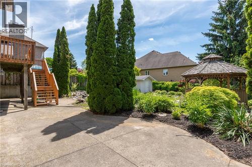 Expansive concrete patio with a wooden deck and stairs, surrounded by mature trees, a garden gazebo, and lush landscaping - 23 Susan Drive, Hamilton, ON 