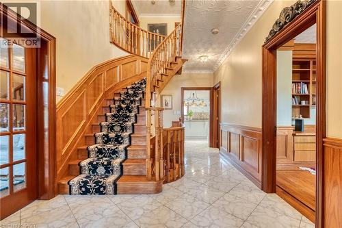 Grand entryway featuring a curved wood staircase with a decorative runner, marble-finish tile flooring, wood paneling, and a built-in wood-finish shelving unit - 23 Susan Drive, Hamilton, ON 