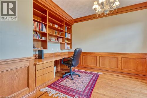 Sophisticated home office featuring rich wood cabinetry with integrated desk workspace, built-in shelving for extensive book storage, wainscoting detail, hardwood flooring, and a professional ergonomi - 23 Susan Drive, Hamilton, ON 