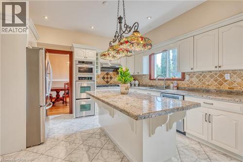 Kitchen featuring white cabinetry, stone countertops, a tiled backsplash, built-in stainless steel appliances, and a central island - 23 Susan Drive, Hamilton, ON 