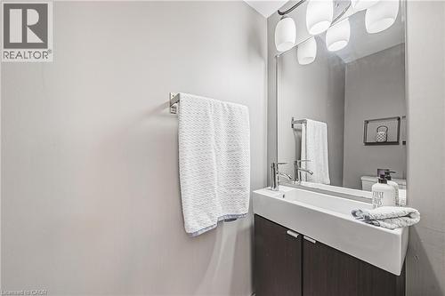 Vanity with an integrated rectangular sink, wood-finish cabinetry, chrome fixtures, and a mirrored wall - 266 Limeridge Road E Unit# 3, Hamilton, ON 