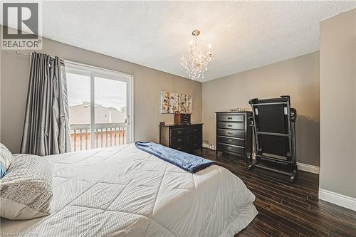 Sliding glass door opening to a private balcony with wood railing, dark wood-finish flooring, and a crystal chandelier - 266 Limeridge Road E Unit# 3, Hamilton, ON 