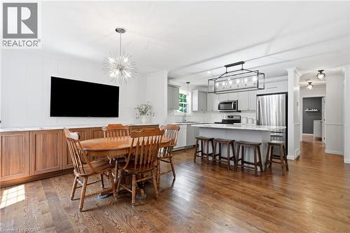 Open-concept kitchen and dining area featuring wood-finish flooring, a kitchen island with seating, stainless steel appliances, and updated light fixtures - 72 Crestlynn Crescent, Simcoe, ON 