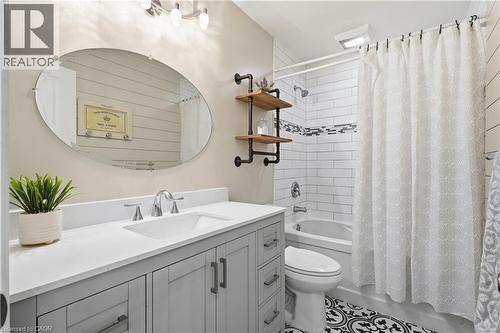 Bathroom featuring a light gray vanity with a white countertop and integrated sink, an oval frameless mirror, subway tile shower surround with an accent band, a built-in tub, and black and white patte - 72 Crestlynn Crescent, Simcoe, ON 