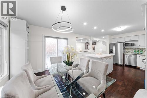 Open-concept dining area featuring a contemporary lighting fixture, wood-finish flooring, and white built-in cabinetry - 495 Brigantine Drive, Waterloo, ON 