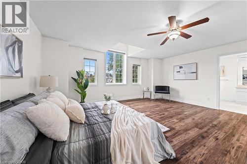 Spacious room featuring wood-finish flooring, multiple windows, a ceiling fan with integrated lighting, and an open doorway to a bathroom with tile flooring - 495 Brigantine Drive, Waterloo, ON 