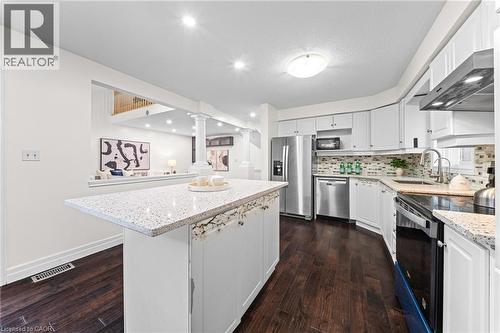 Kitchen featuring a central island with a light-toned countertop, white cabinetry, dark wood-finish flooring, stainless steel appliances, and a tiled backsplash - 495 Brigantine Drive, Waterloo, ON 